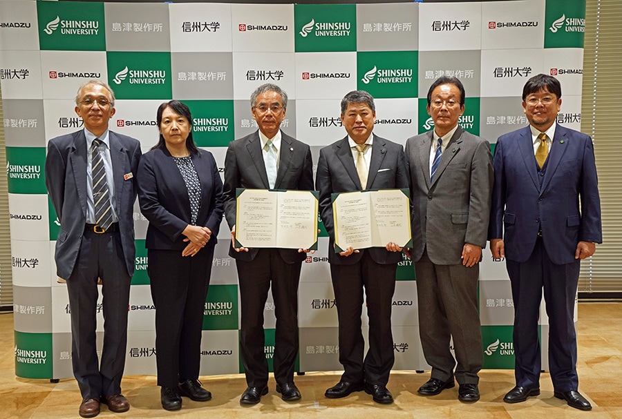 From the left is Deputy Manager Junichi Masuda, Healthcare Solution Unit, Solutions Center of Excellence, Analytical & Measuring Instruments Division, Shimadzu Corporation; Corporate Officer and Deputy General Manager Naomi Okazaki, Analytical & Measuring Instruments Division, Shimadzu Corporation; President & CEO Yasunori Yamamoto, Shimadzu Corporation; President Soichiro Nakamura, Shinshu University; Trustee (Research and Industry-Academia-Government Collaboration) and Vice-President Chisato Mukai, Shinshu University; and Katsuya Teshima, Director of Institute for Aqua Regeneration