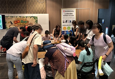 Children braided ropes out of strings under the watchful eyes of shimadzu staff and guardians